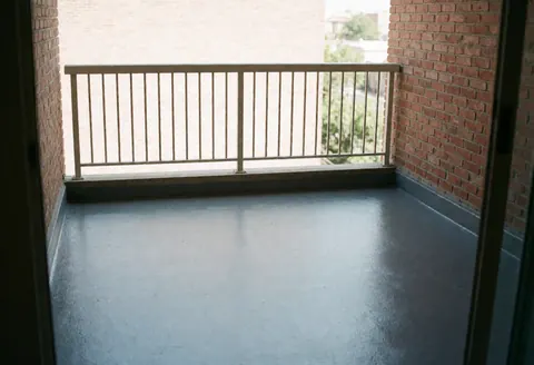 Vue d'un balcon fini avec une barrière en briques rouges et des murs gris, offrant un espace extérieur propre et moderne avec une fenêtre et une lumière naturelle.