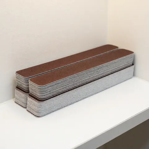 Une pile soignée de limes à ongles aux textures visibles repose sur une surface blanche propre, évoquant un environnement professionnel et hygiénique pour salon de manucure.