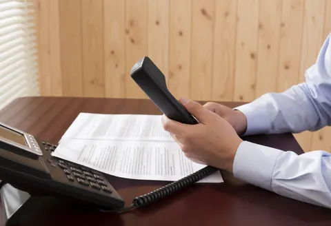 Un avocat en réunion professionnelle sérieuse, assis à un bureau en bois avec des documents et un téléphone, dans un environnement de bureau moderne.