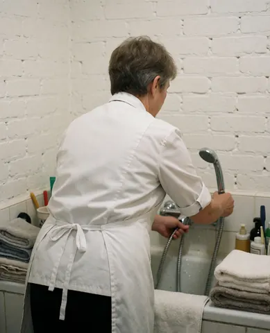 Un groomer professionnel règle la douche au-dessus d'une baignoire, avec des serviettes rangées et des murs en briques blanches, montrant un environnement propre pour le soin canin.