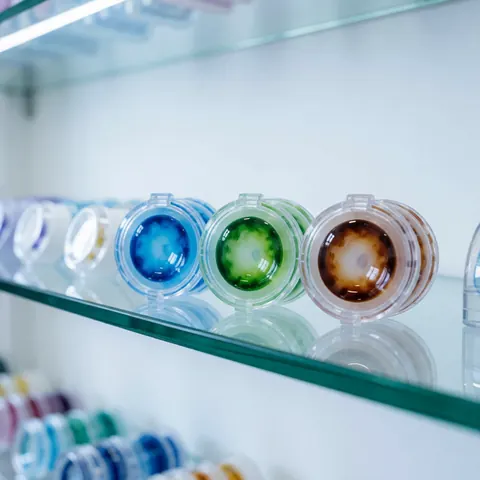 Des lentilles de contact colorées disposées sur des étagères en verre dans une optique moderne, avec un arrière-plan flou montrant d'autres produits de soin visuel.