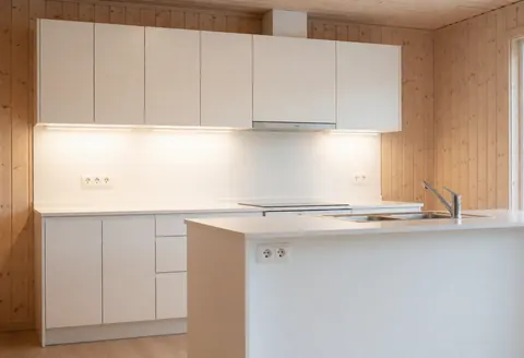 Cuisine moderne et épurée dotée d'armoires blanches, de panneaux en bois, d'un éclairage LED intégré, sans présence humaine, adaptée aux professionnels de l'électricité.