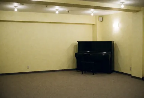 Intérieur d'un bar vide avec un piano noir dans un coin, des murs jaune pâle, une lumière chaleureuse, idéal pour des événements musicaux.