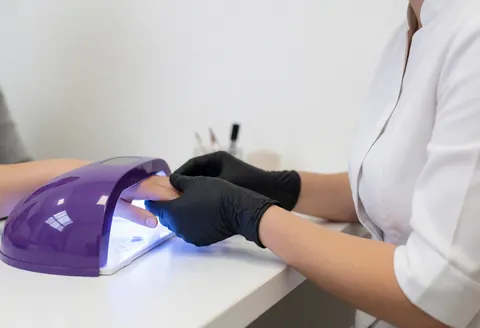Une manucure professionnelle utilise une lampe uv pour durcir le vernis gel sur les ongles d'une cliente dans un salon de beauté.