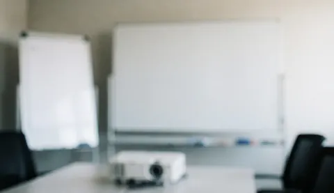 Vue d'une salle de réunion professionnelle équipée d'un grand tableau blanc, d'un projecteur et de chaises autour d'une table.