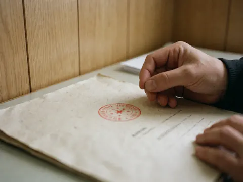 Gros plan de mains posant un cachet administratif sur une paperasse posée sur un bureau en bois.