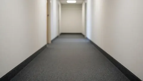 Arrière-plan flou d'un couloir intérieur avec des murs blancs et une moquette grise, idéal pour superposer du texte.