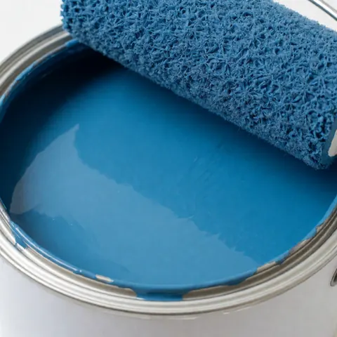 Un rouleau de peinture applique une couche de peinture intérieure bleue brillante sur un mur, illustrant un projet de rénovation ou de décoration pour les entreprises.