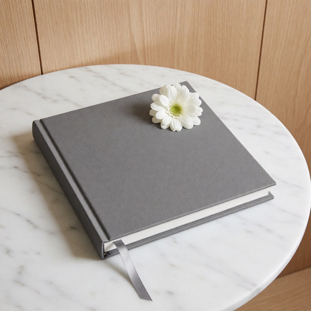 Vue de dessus d'un album photo fermé aux couvertures en marbre gris et blanc orné d'une fleur blanche, posé sur une surface en bois naturel.