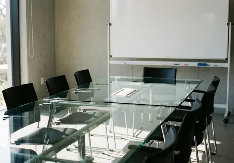 Salle de réunion moderne vide avec table en verre, chaises noires et tableau blanc sur mur en béton, idéale pour les affaires et le travail productif.