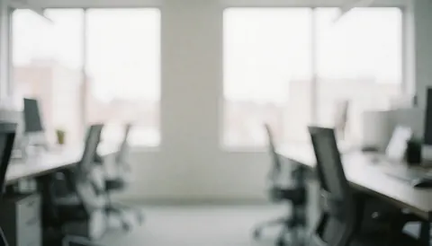 Un espace de travail moderne et aéré comprenant un bureau, une chaise et une grande fenêtre laissant entrer la lumière naturelle sur un fond blanc et gris flou.