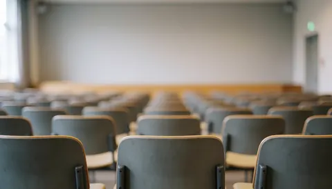 Arrière-plan flou d'une salle de classe universitaire avec des chaises et un tableau blanc, idéal pour superposer du texte.