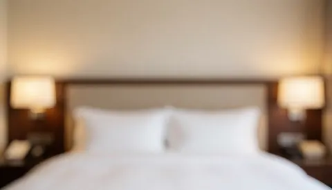 Arrière-plan d'une suite hôtelière montrant un lit et des lumières douces, idéal pour textes promotionnels, évoquant confort et luxe.