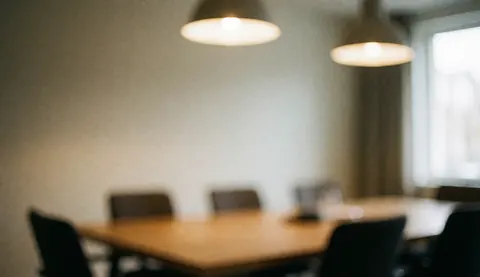 Vue d'un espace de réunion professionnel avec une table en bois, des chaises et une lumière naturelle tamisée, servant de fond pour du texte ou de la publicité.