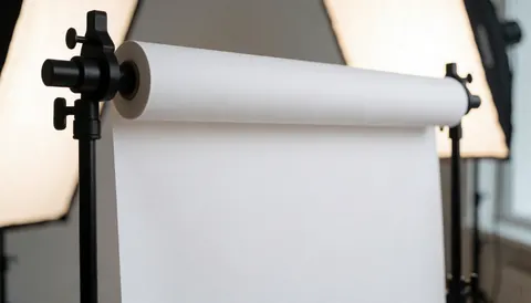 Fond blanc avec rouleau de papier dans un studio, éclairage doux et professionnel, idéal pour le marketing et la présentation de produits.