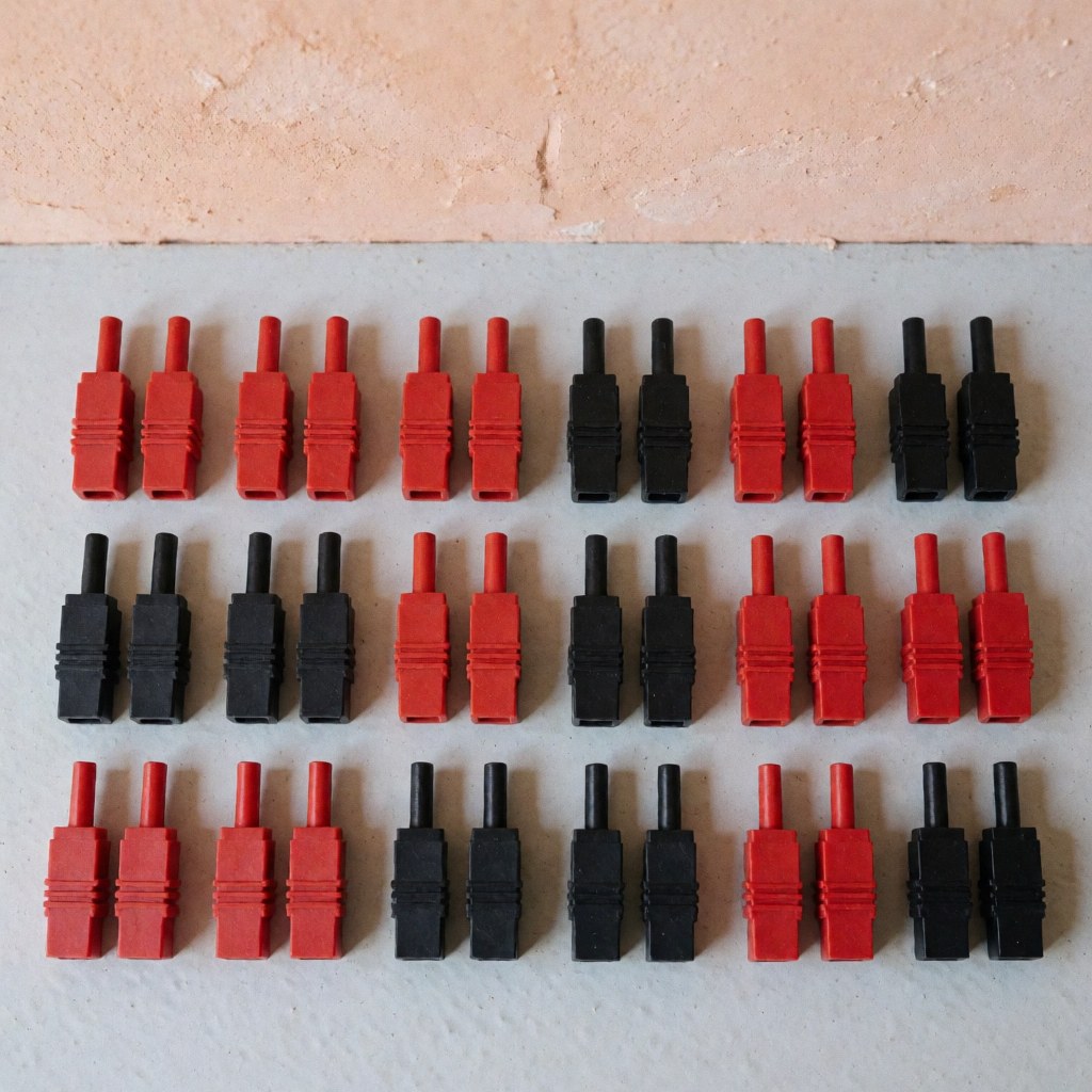 Vue de dessus montrant des connecteurs électriques disposés sur une surface grise avec un mur terracotta en arrière-plan sous éclairage naturel.