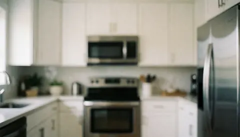 Armoires de cuisine blanches et électroménager en acier inoxydable sur fond flou neutre pour texte ou présentation professionnelle.
