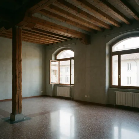 Intérieur d'une salle restaurée mettant en valeur des poutres en bois apparentes, un sol en terrazzo, des fenêtres et des arcs sur les murs.