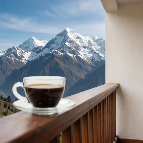 Une tasse de café posée sur une terrasse en bois offrant une vue imprenable sur des montagnes enneigées sous un ciel bleu éclatant.