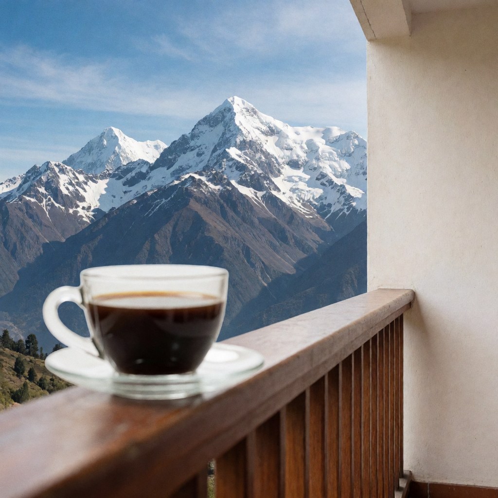 Une tasse de café posée sur une terrasse en bois offrant une vue imprenable sur des montagnes enneigées sous un ciel bleu éclatant.