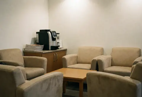 Espace d'accueil chaleureux doté de fauteuils beiges, d'une table en bois et d'un distributeur de café, conçu pour les clients de cabinets comptables.