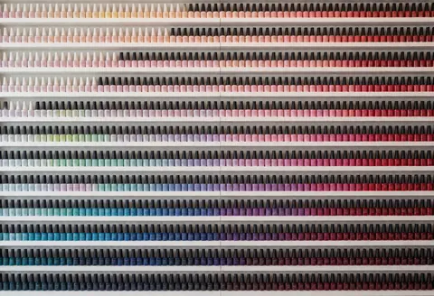 Étagères remplies de centaines de bouteilles de vernis à ongles organisées en dégradé du pastel au rouge, idéal pour un salon professionnel.