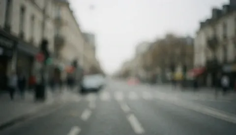 Fond de rue urbaine flou en tons gris, idéal pour textes ou graphiques professionnels. Bâtiments et chaussée flous sous lumière diffuse.