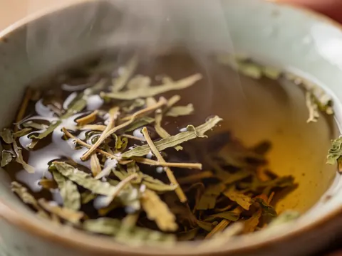 Gros plan d'une tasse en céramique contenant du thé chaud aux herbes, des feuilles flottent à la surface tandis que la vapeur s'élève, évoquant détente et bien-être.