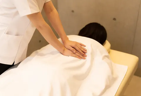 Un thérapeute en uniforme blanc applique un massage sur le dos d'un client recouvert d'une serviette blanche sur une table de massage dans un cadre apaisant.