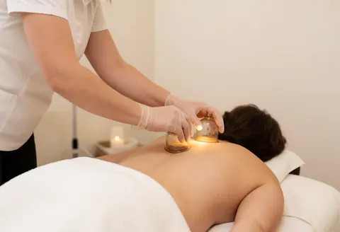 Un thérapeute effectue une séance de cupping sur le dos nu d'un client allongé sur une table de massage dans un cadre intérieur lumineux et apaisant.