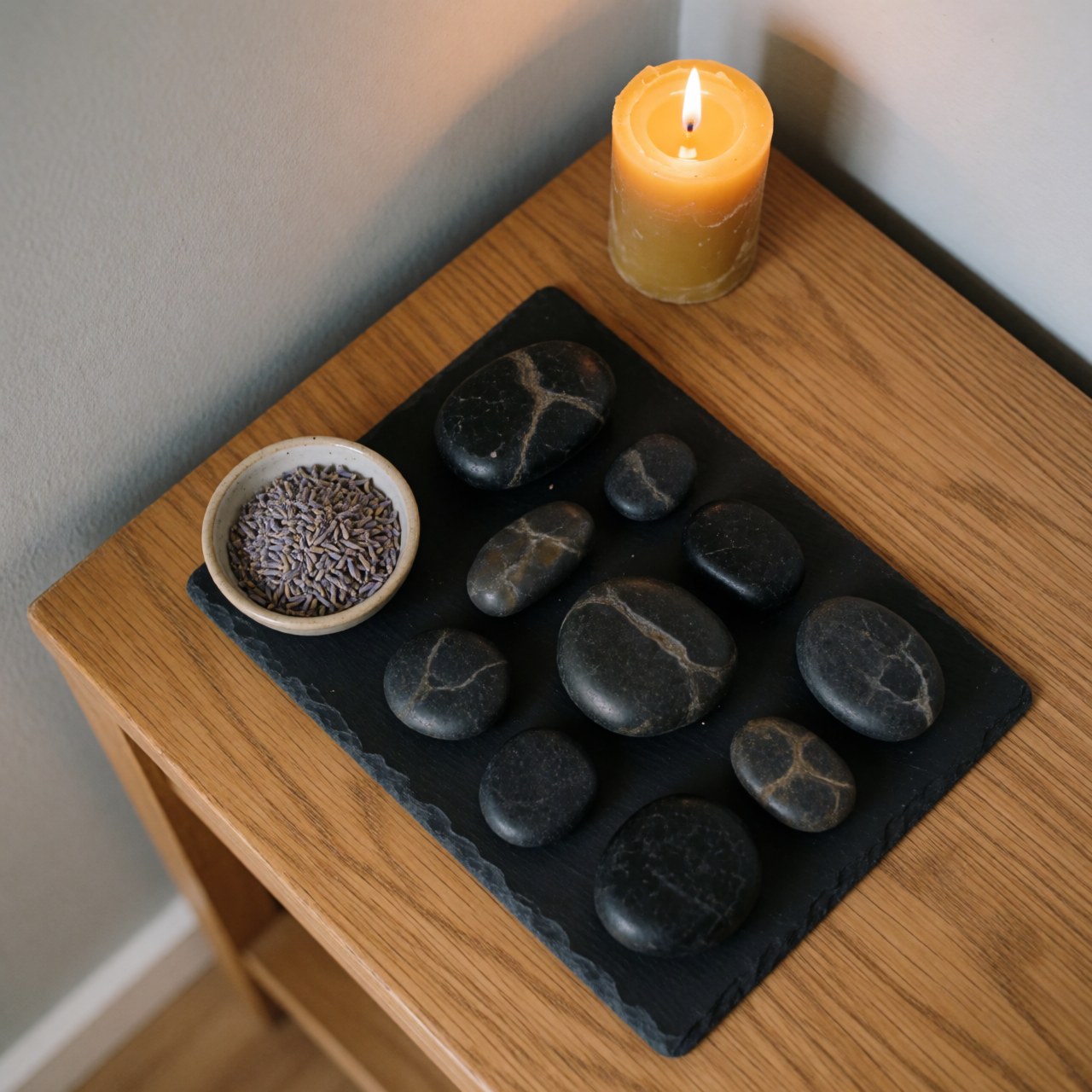 Des pierres volcaniques noires et chaudes disposées sur une table en bois, accompagnées d'une bougie et d'un bouquet de lavande, créant une ambiance de bien-être et de relaxation.