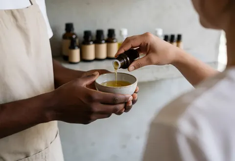 Mains d'un professionnel versant des huiles essentielles dans un bol en céramique pour une séance de massage thérapeutique.