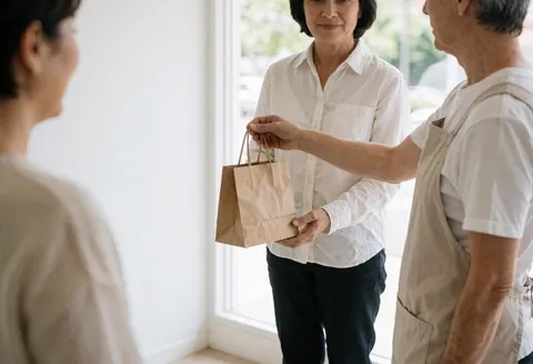 Un thérapeute en massage remet une pochette à un client dans un intérieur lumineux, évoquant calme et professionnalisme.