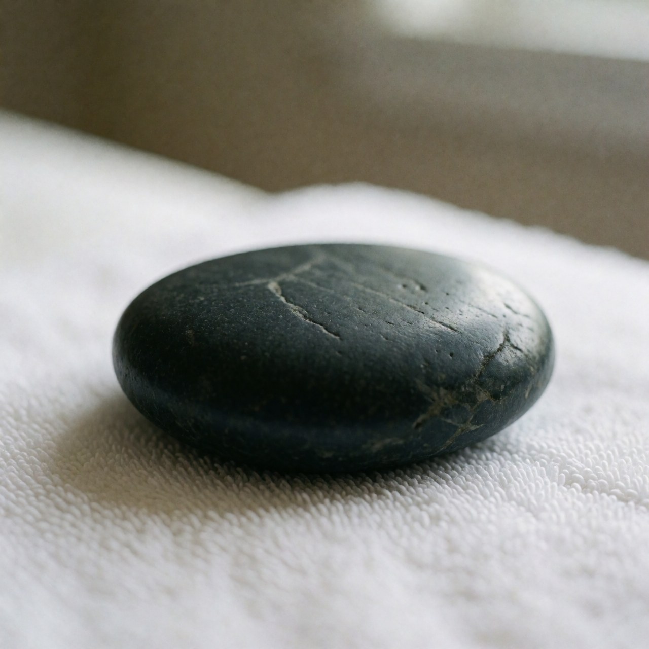 Gros plan d'une pierre de basalte utilisée pour le massage thérapeutique posée sur une serviette blanche, évoquant la détente et le bien-être dans un cadre professionnel.