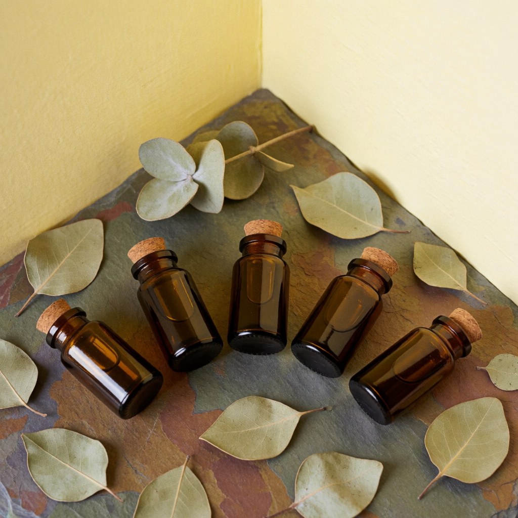 Vue de dessus sur des flacons en verre contenant des huiles essentielles disposés avec des feuilles sèches et une pierre naturelle.