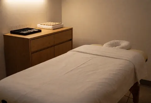 Intérieur calme et minimaliste d'une salle de traitement d'acupuncture avec lit de massage, draps blancs et éclairage doux.