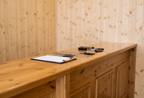Un comptoir en bois clair et poli dans une boutique de chaussures, avec des outils, un carnet et des murs en panneaux de bois.