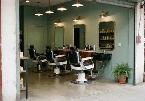Vue d'un salon de barbier moderne avec des fauteuils vintage, des miroirs, des murs verts et une plante dans le coin.