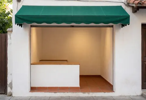 Façade de commerce avec auvent vert, murs blancs et sol en carreaux de terre cuite, éclairage chaleureux et ambiance conviviale.