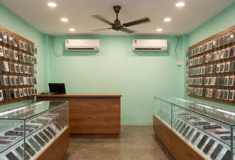 Intérieur d'un magasin de téléphones avec murs verts, comptoirs en verre, climatiseur, téléphones en boîtes et vitrines, ambiance propre et organisée.
