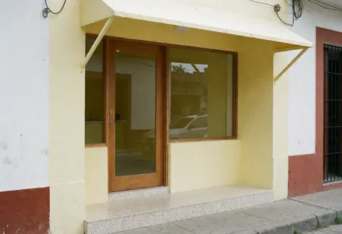 Vue de la façade extérieure d'un cabinet comptable avec une porte en bois, un mur jaune et un escalier en terrazzo sous un auvent.