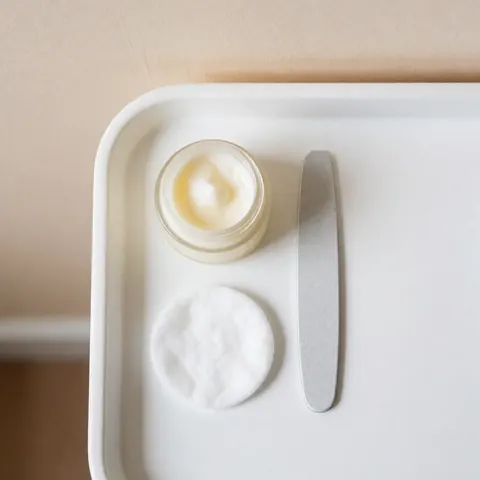 Plateau blanc avec crème pour les pieds, lime à ongles et chiffon en coton pour le soin des pieds et des ongles.