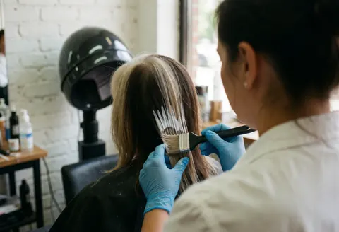Coiffeuse appliquant du colorant sur les cheveux avec un pinceau dans un salon de coiffure moderne.