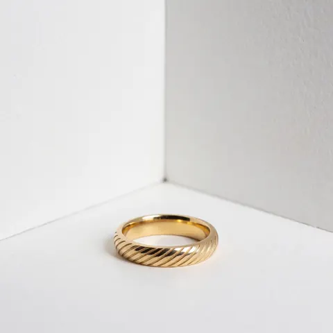 Une bague en or avec une gravure personnalisée visible sur un fond blanc minimaliste mettant en valeur le détail et la texture du métal.