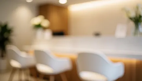 Vue d'un espace de réception moderne avec chaises, table en bois, éclairage doux et plantes vertes sur un fond blanc chaleureux.