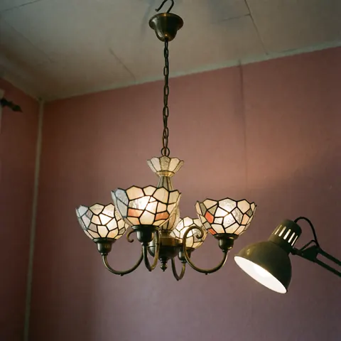 Chandelier en cristal aux motifs géométriques, illuminé par une lampe de travail, suspendu devant un mur rose dans un atelier d'artisanat.