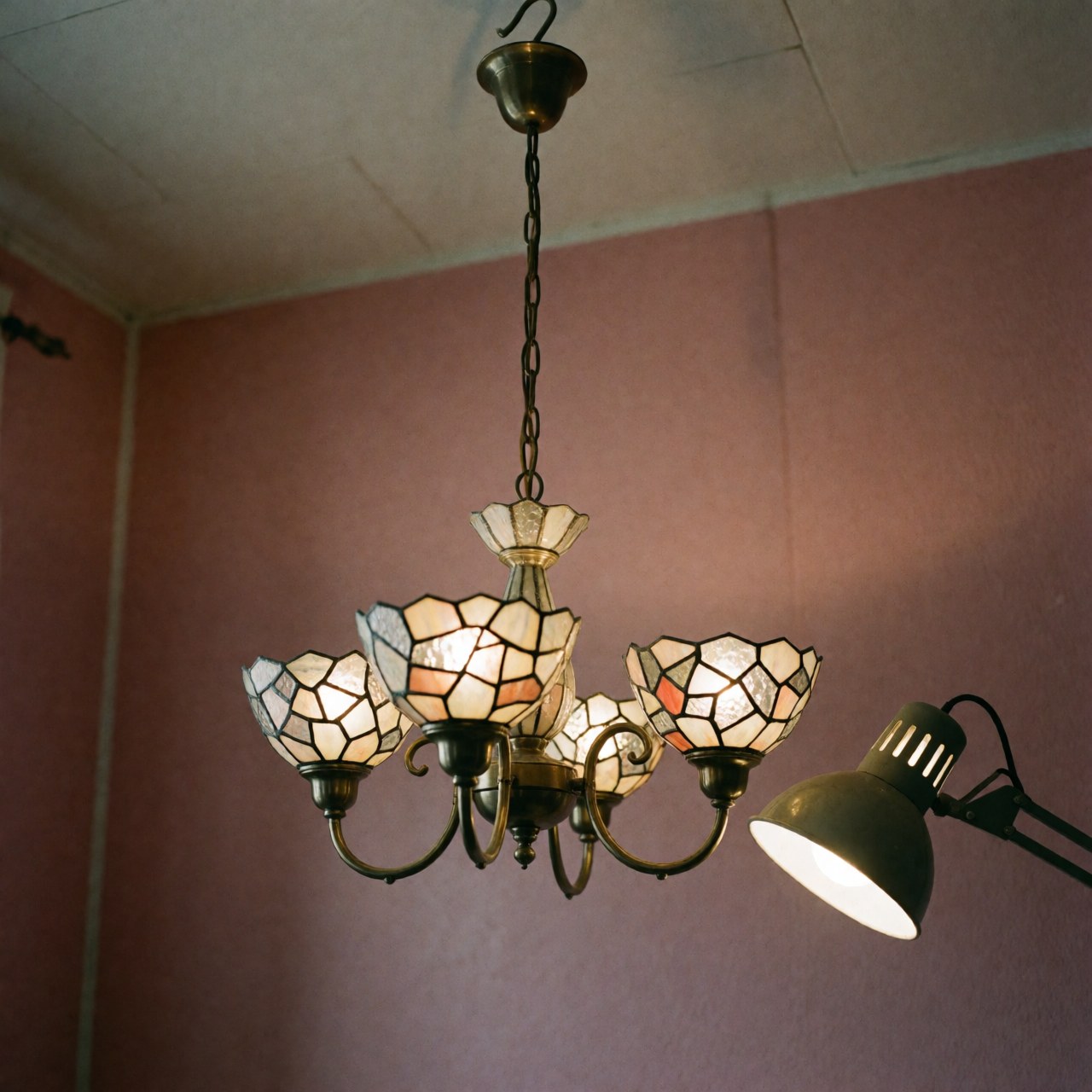 Chandelier en cristal aux motifs géométriques, illuminé par une lampe de travail, suspendu devant un mur rose dans un atelier d'artisanat.