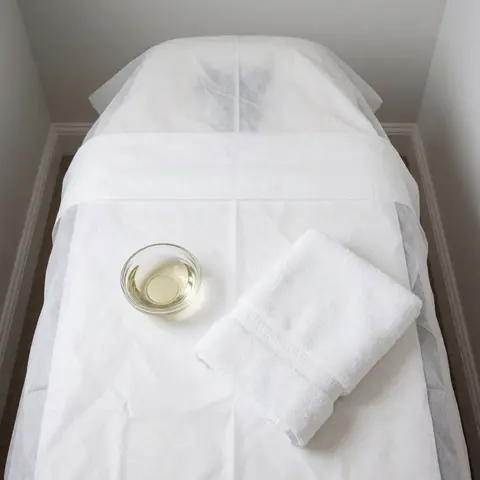 Une table de massage recouverte d'une serviette blanche, accompagnée d'un petit bol d'huile et d'une serviette pliée, prête pour une séance de thérapie.