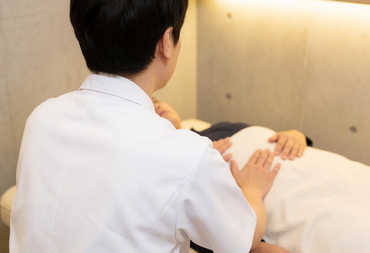 Ostéopate en blouse blanche réalise un ajustement viscéral sur l'abdomen d'un patient allongé sur une table, dans un cadre professionnel et apaisant.