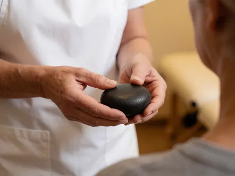 Thérapeute aux mains propres tenant une pierre de basalte chaude et douce, prête à appliquer un massage thérapeutique sur l'épaule d'un patient dans une salle relaxante.